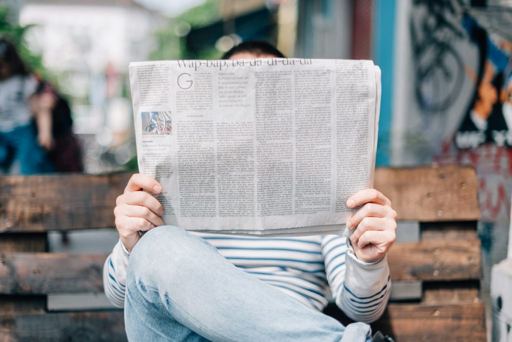 Zeitungen & Zeitschriften Person sitzt auf einer Bank und liest eine Zeitung.